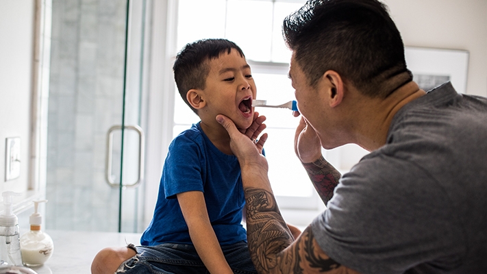 A father helps his son brushing his teeth; image used for HSBC Medical Insurance.