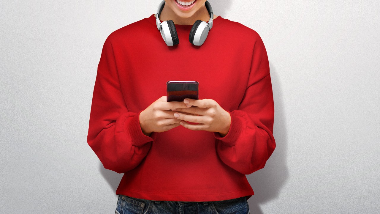 Smiling young guy with a headset around his neck holding his mobile phone; image used for HSBC One