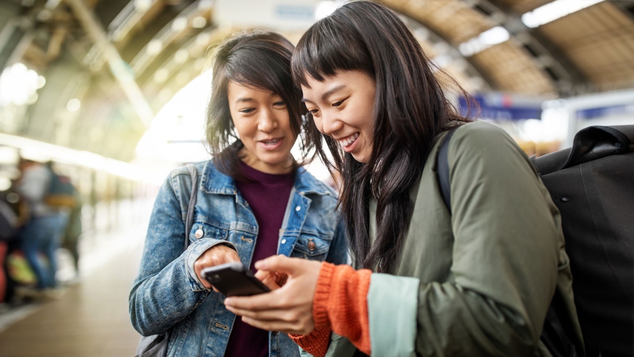 两位女士高兴地看着手机；图片使用于关于汇丰保险“创新电子平台”。
