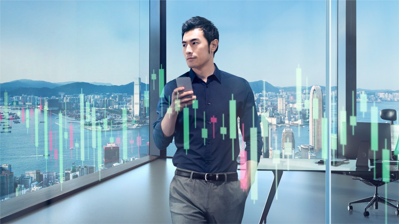 A businessman standing next to the window of his top floor office is using his mobile; image used for HSBC Top Trader Club.